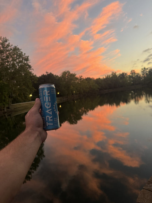 Holding a Trager Blue Raspberry can at sunset by the lake